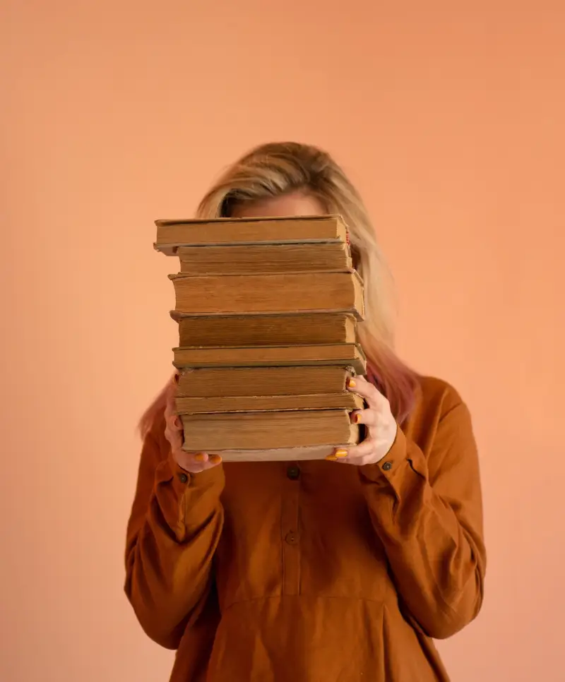 woman holding a stack of old books in front of her face